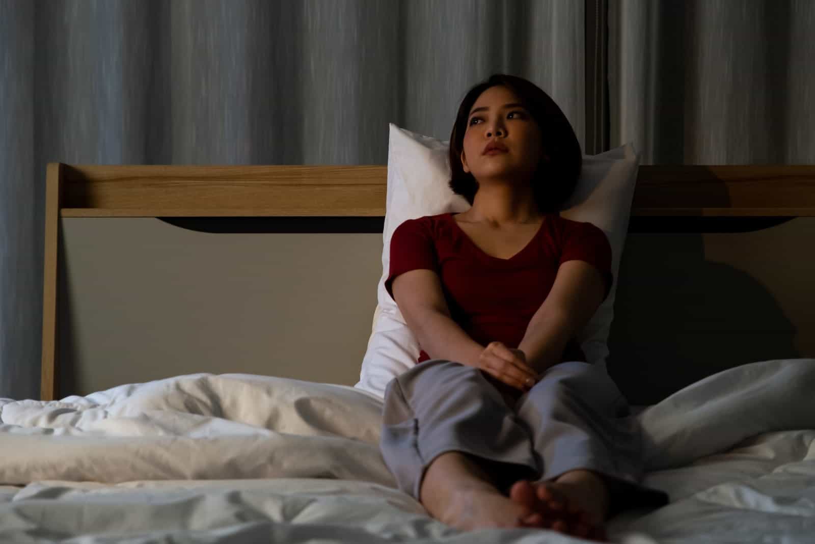 Ein trauriges asiatisches Mädchen sitzt im Bett und denkt nach