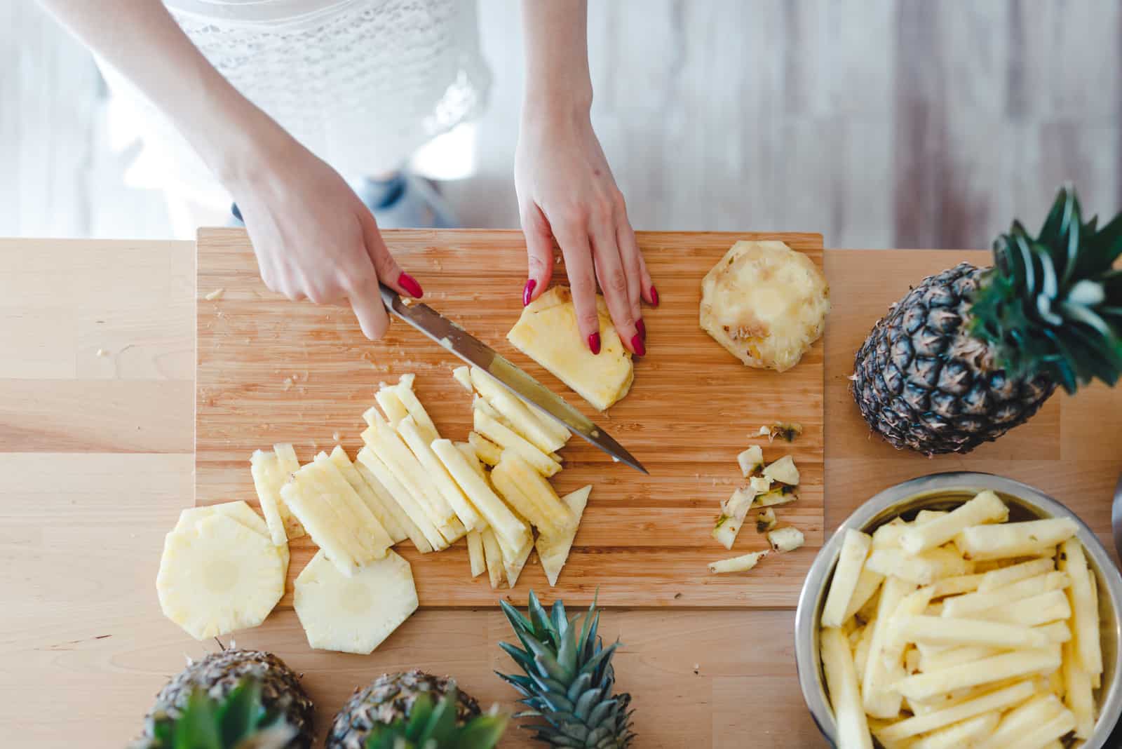 Frau geschnittene Ananas mit einem Messer auf dem Küchentisch
