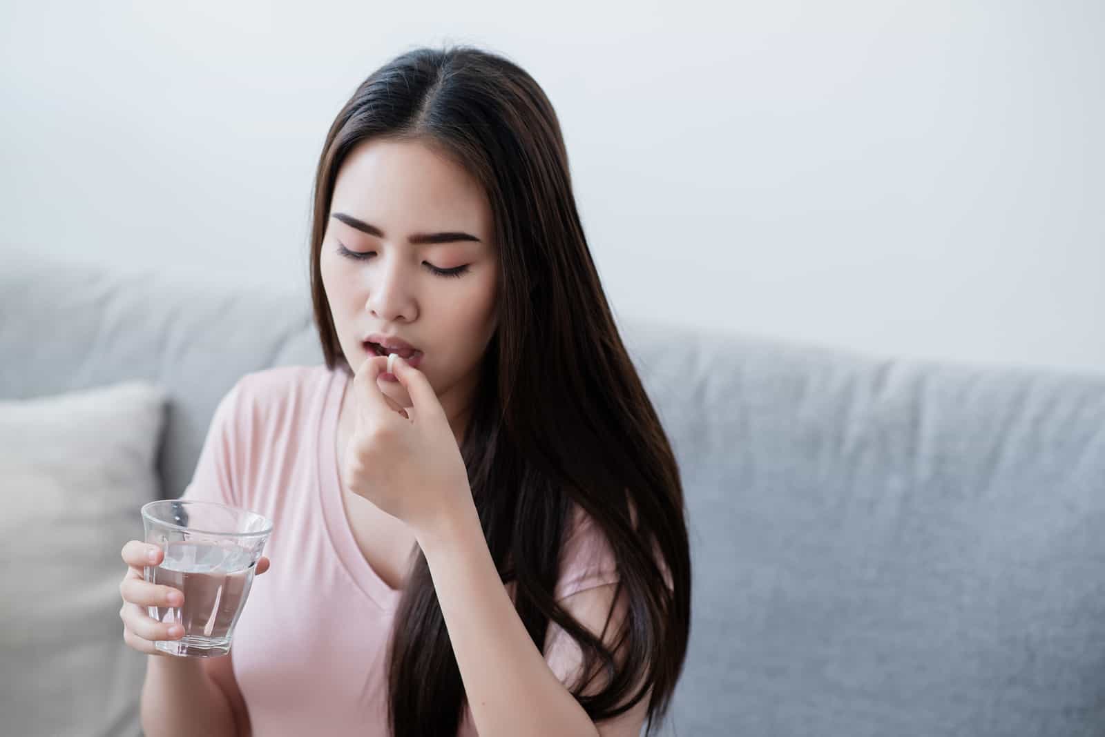 Kranke Frau trinkt Tabletten mit einem Glas Wasser in der Hand