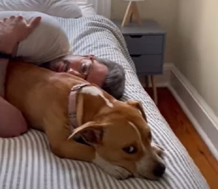 Ein Mann umarmt einen Hund im Bett