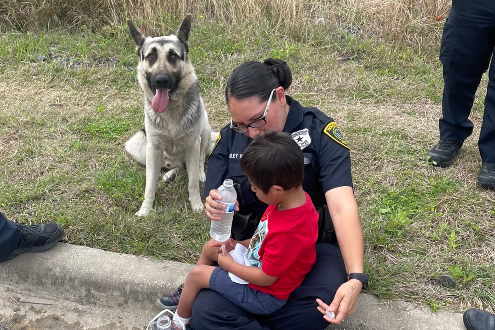 Polizistin und Junge und Hund sitzen am Straßenrand