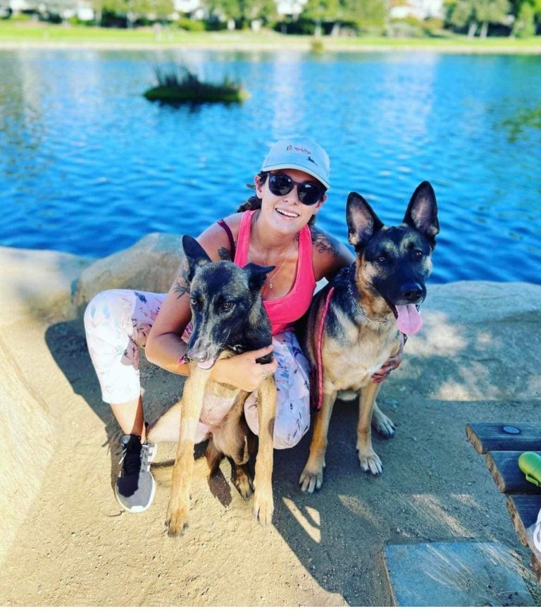 Zwei Malinois-Hunde und ihre Besitzerin am See