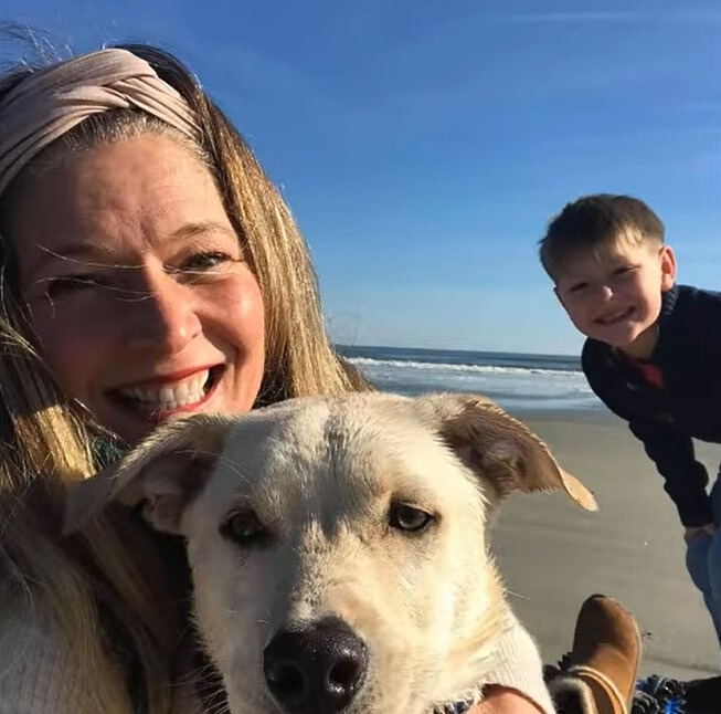 Laechelnde Frau mit einem Kind und einem Hund am Strand